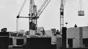 Black and white image of a construction site with cranes and workers, emphasizing urban industrial development.